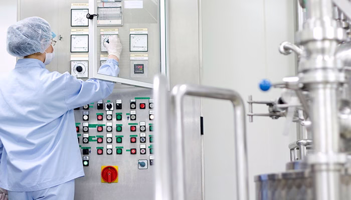 Operator in clean room garment, standing in front of filling equipment.