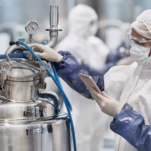Pharmaceutical production staff in clean room garment inspecting a process vessel
