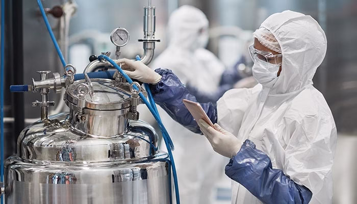 Pharmaceutical production staff in clean room garment inspecting a process vessel